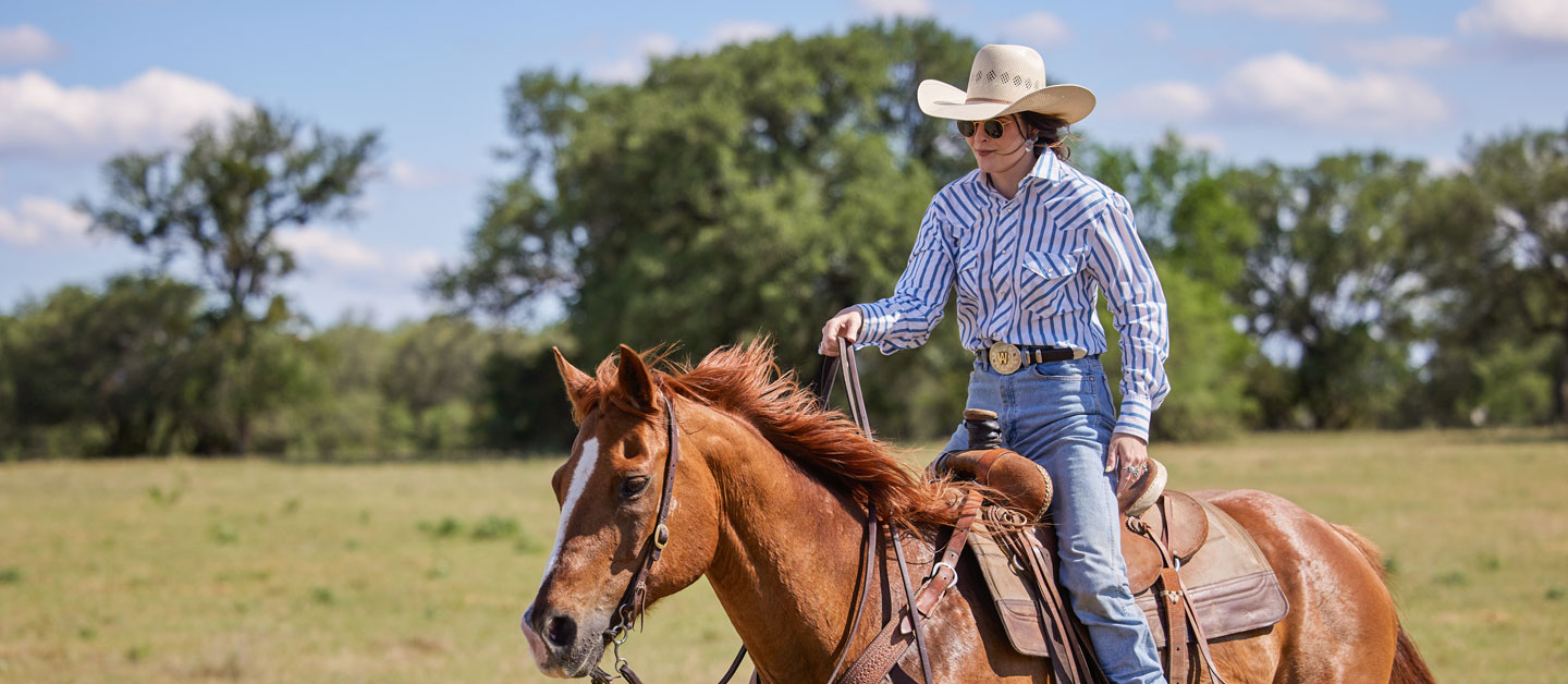 woman riding a horse wearing cowgirl attire.